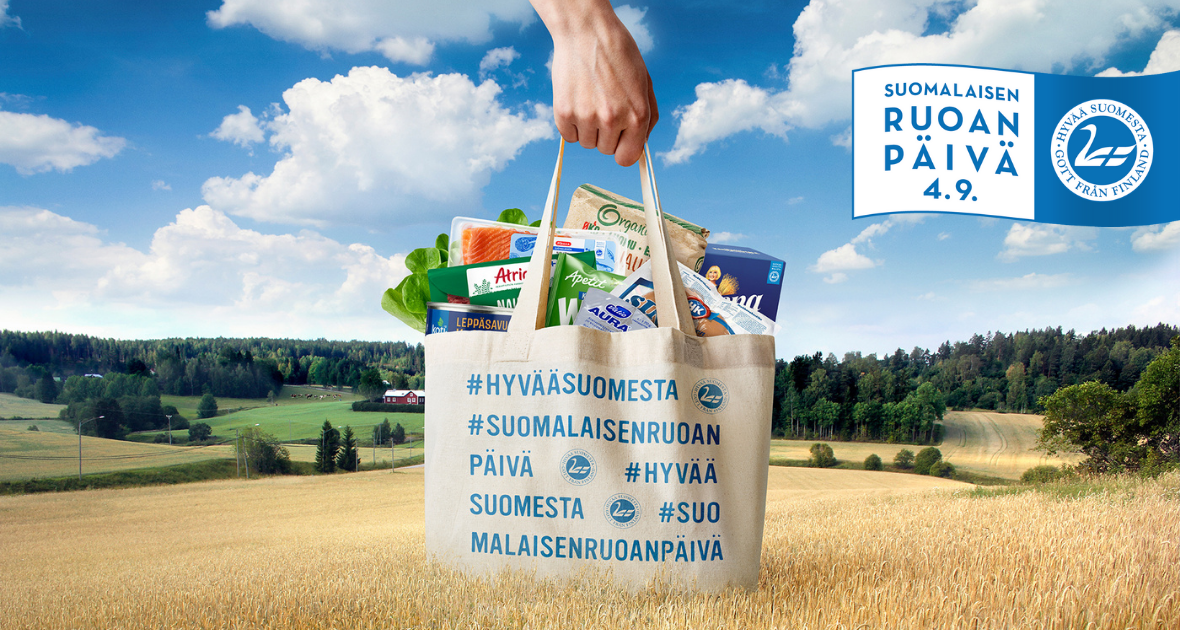 kädessä kangaskassi, jossa suomalaisen ruoan päivä -teksti, taustalla viljapelto
